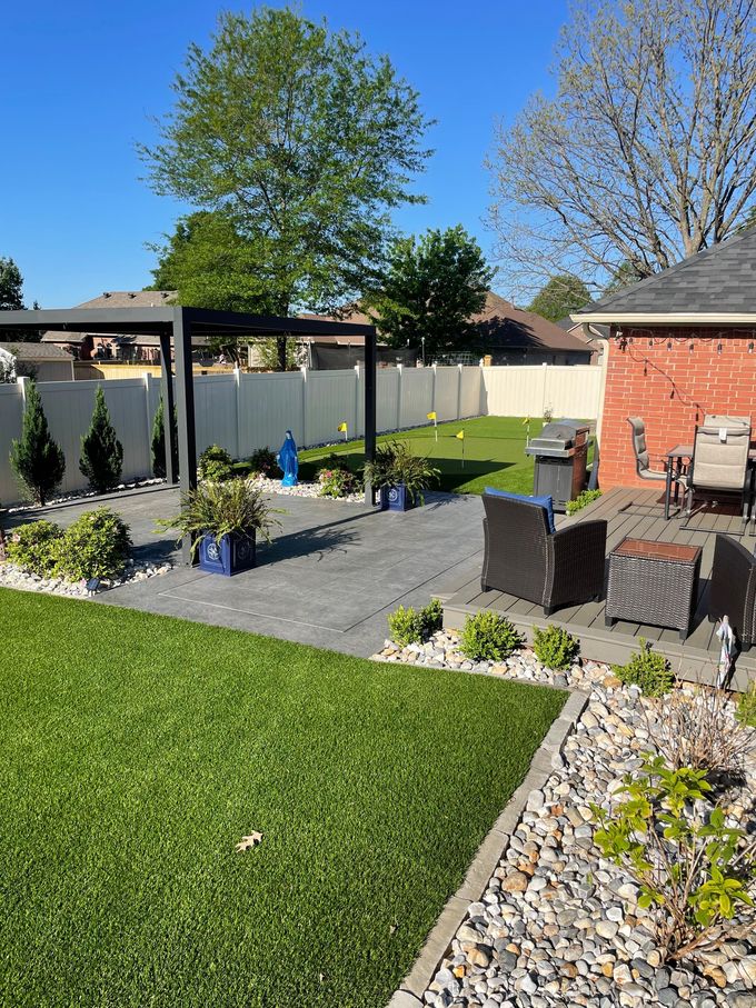 Sunny backyard with patio seating, potted plants, lawn, and a pergola by a brick house