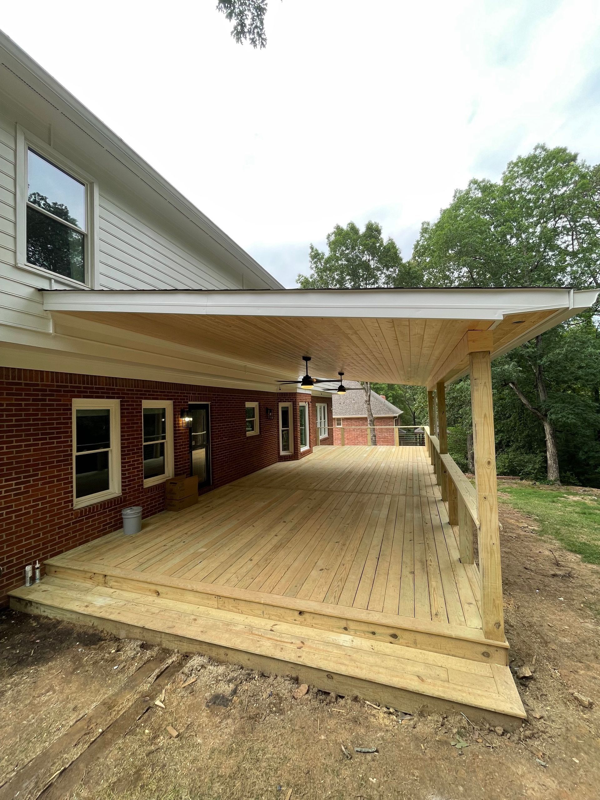 Wooden deck with a covered porch extending from a brick building.