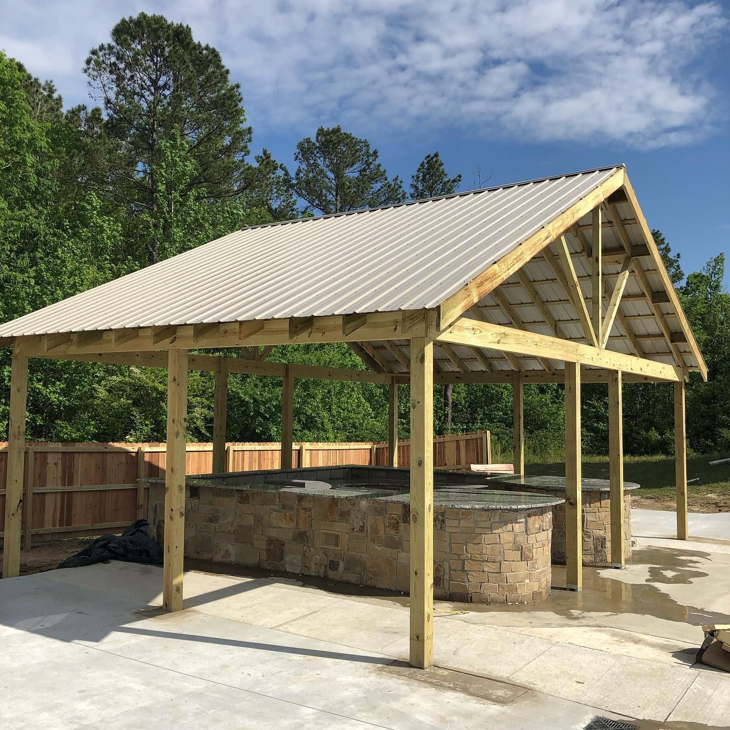 Wooden outdoor pavilion with stone countertops and a metal roof.