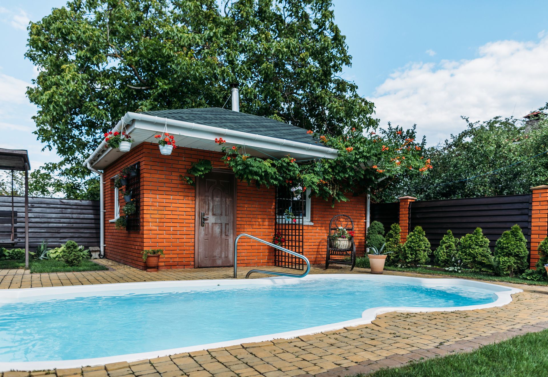 Small pool with adjacent orange brick building, surrounded by greenery under a cloudy blue sky.