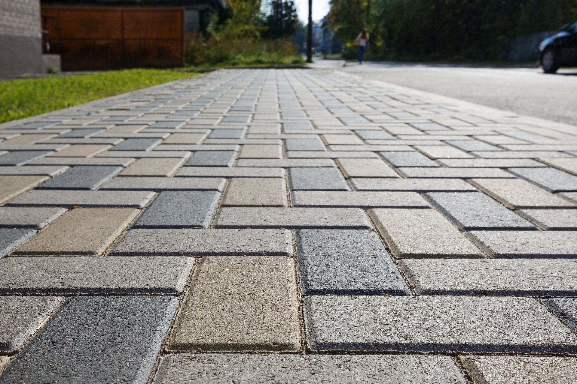 Low-angle view of a paved sidewalk with gray and tan rectangular bricks along a street