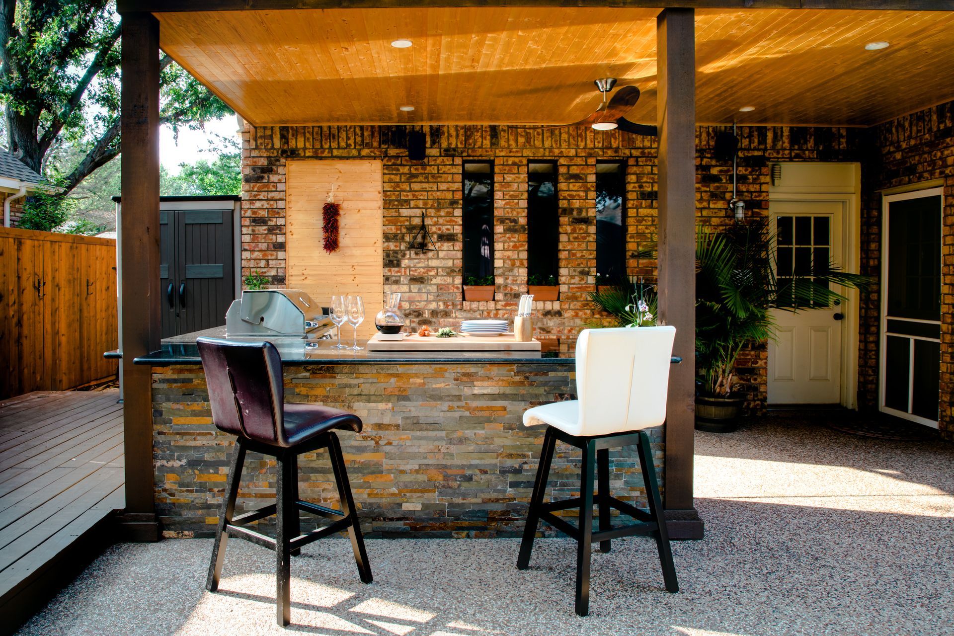 Outdoor kitchen with stone bar, two stools, and wooden pergola in a backyard