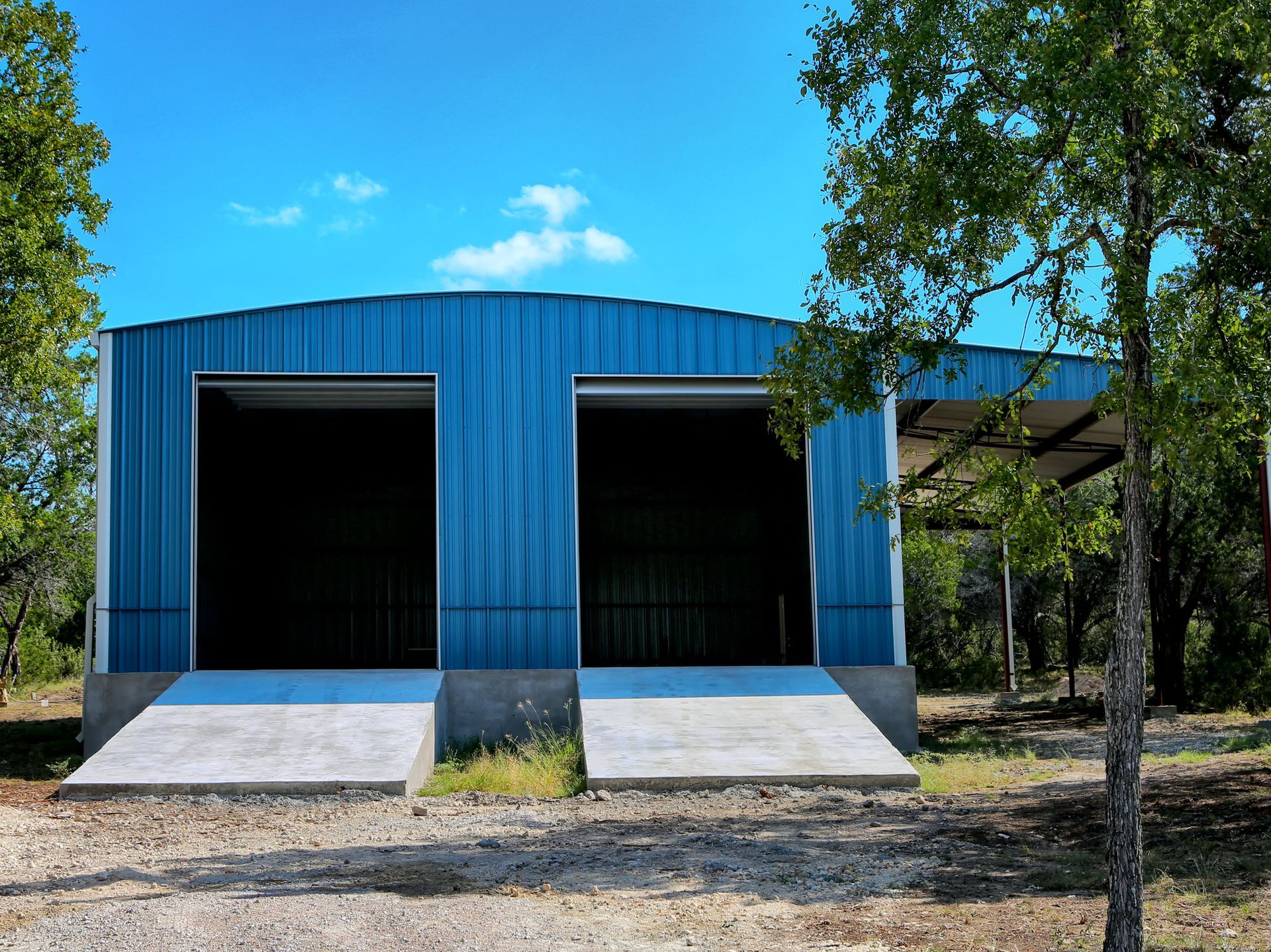 Blue metal building with two open garage doors; concrete ramps; blue sky.