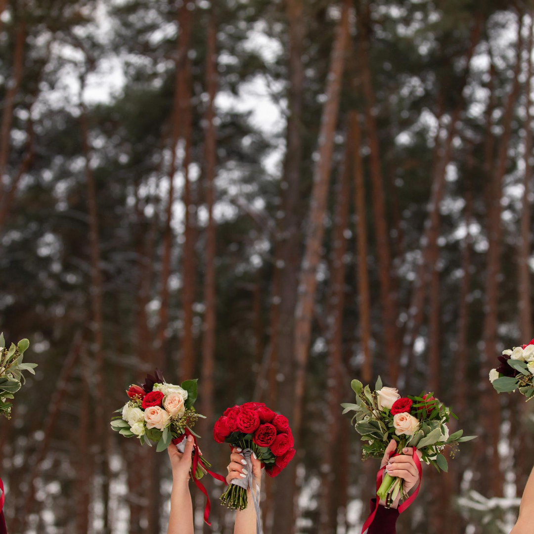 Bridesmaids raise colorful bouquets of roses in a winter forest, blurred background.