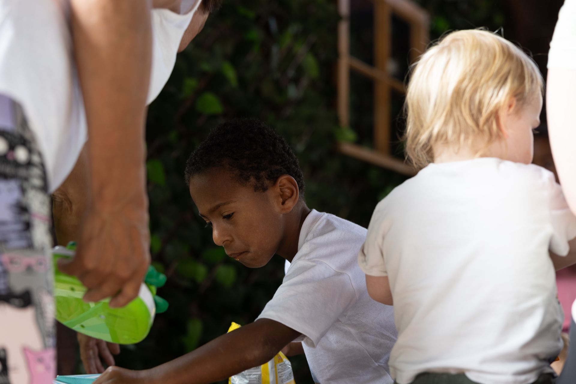 Boy and toddler at a table, both wearing white shirts. Someone holds a green object nearby.