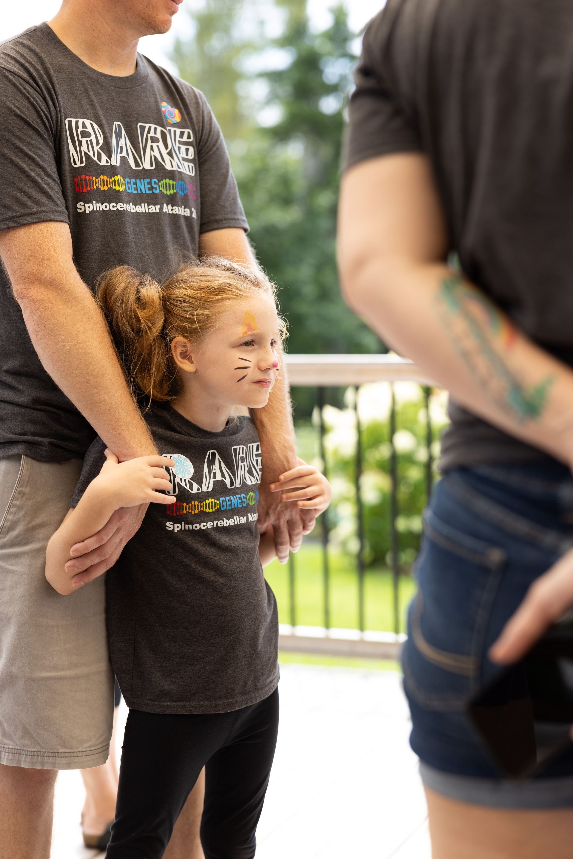 Girl with face paint and pigtails, standing between two adults, wearing a t-shirt that matches the adults.