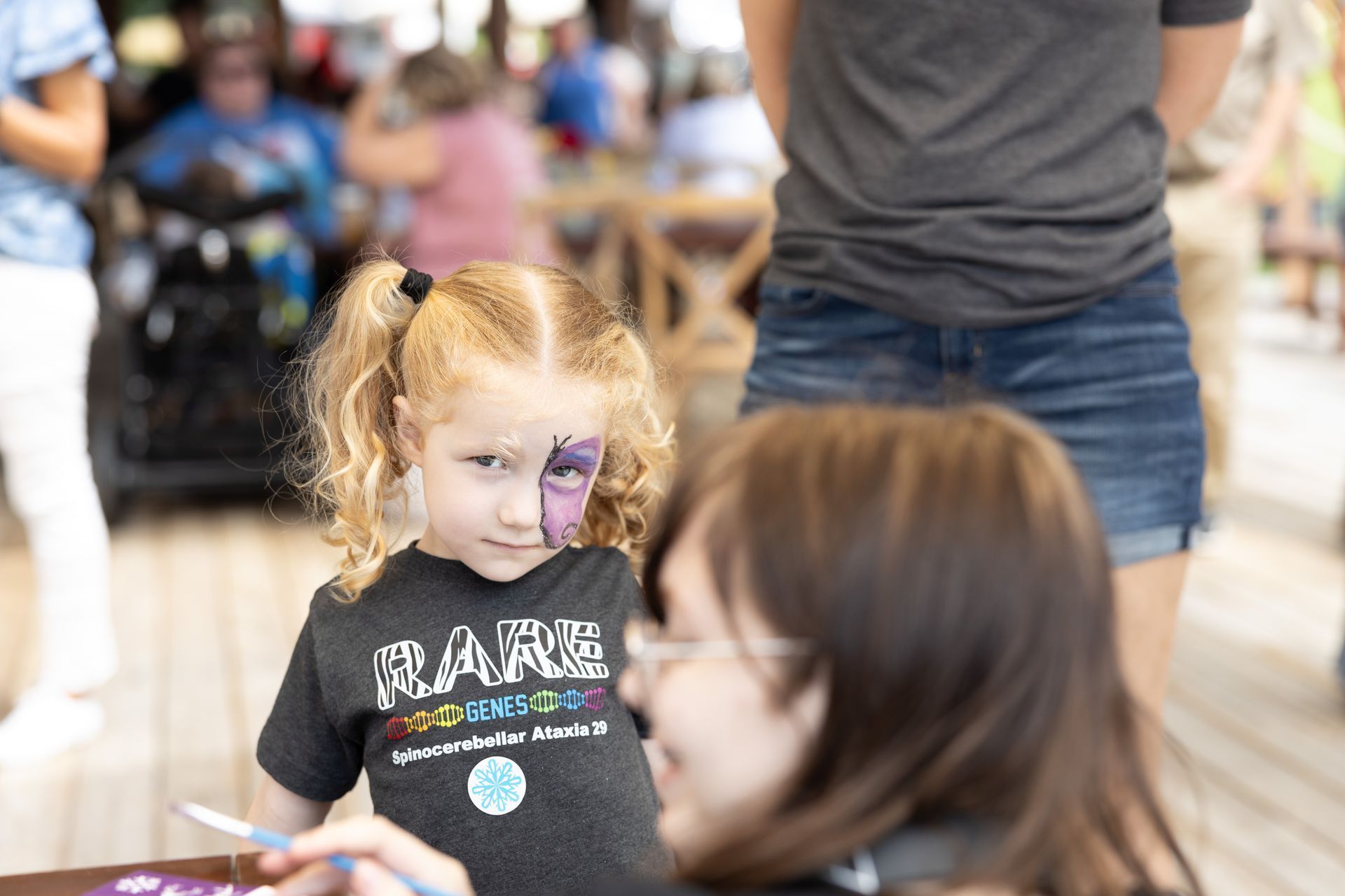 Girl with face paint looks at the artist. Outdoor setting; the girl wears a t-shirt that says