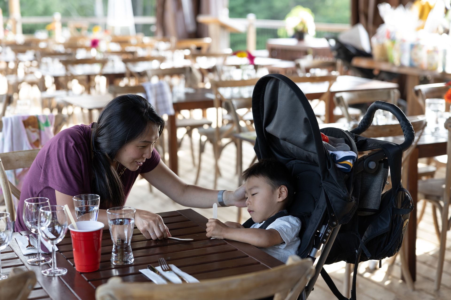 Woman and child at outdoor restaurant. Child in stroller, woman seated at table, looking at child.