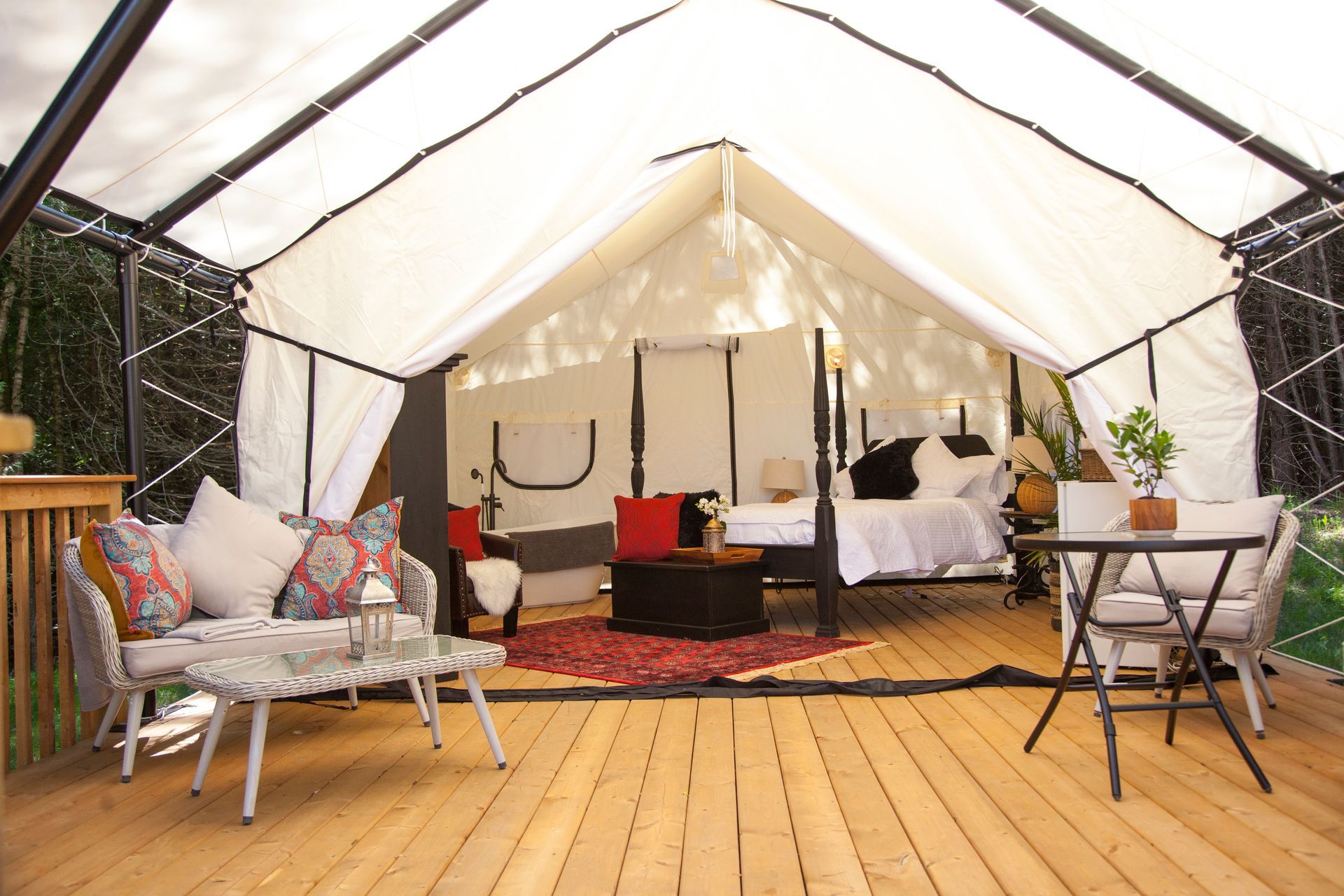 A luxurious glamping tent interior with a bed, furniture, and a wooden deck outside.