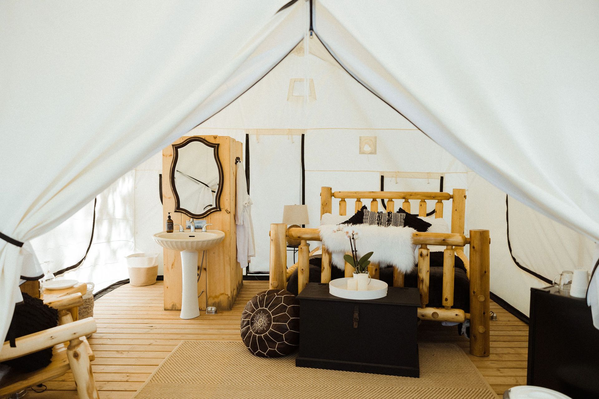 Inside of a glamping tent: wooden bed, sink, cabinet, and rug on a wooden floor.