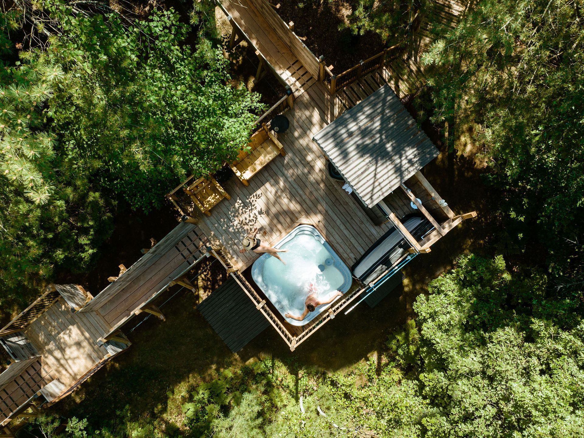 Overhead view of a treehouse with a hot tub on the deck surrounded by trees.