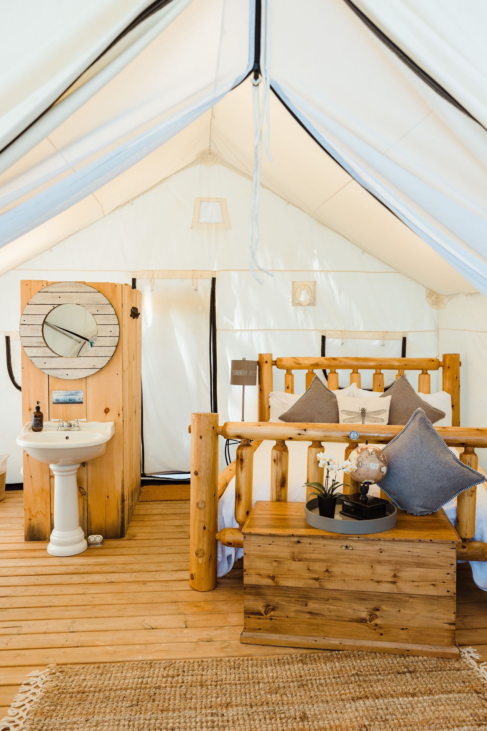 Interior of a glamping tent with a wooden bed, sink, and wood floor.