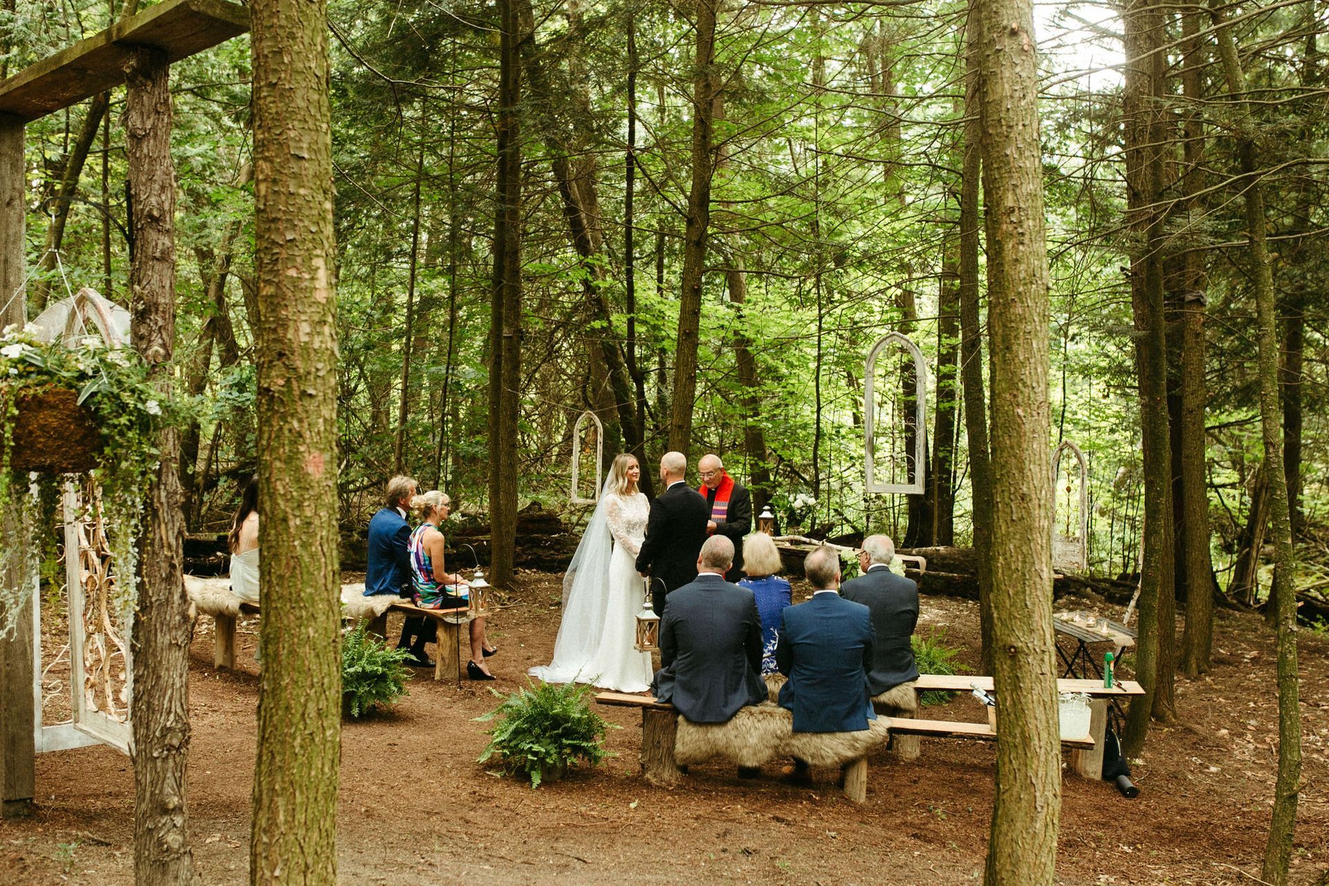 Wedding ceremony in a forest clearing: bride and groom stand before guests near an officiant.
