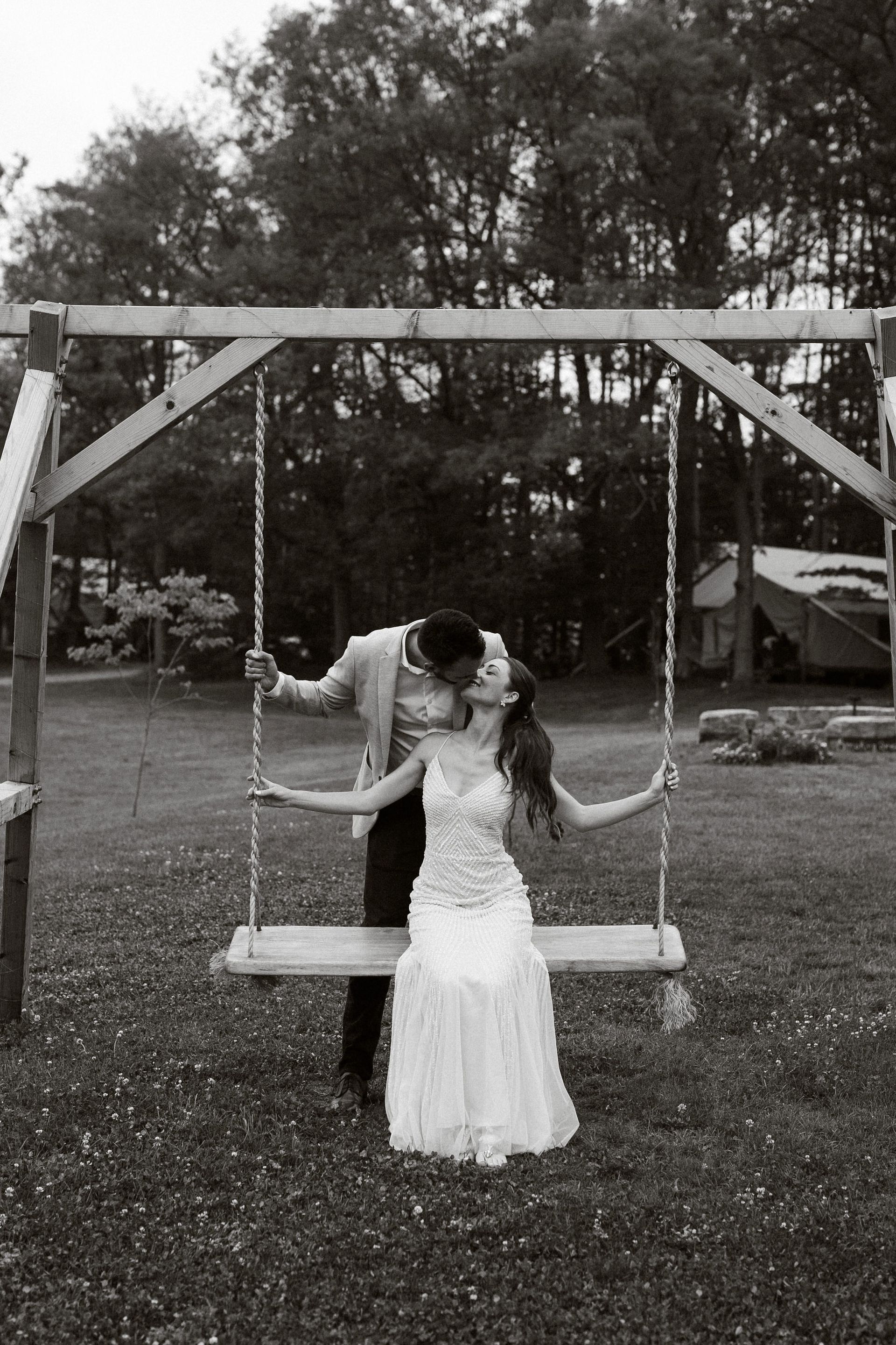 Couple kissing on a swing; man in suit, woman in white dress, outdoors.