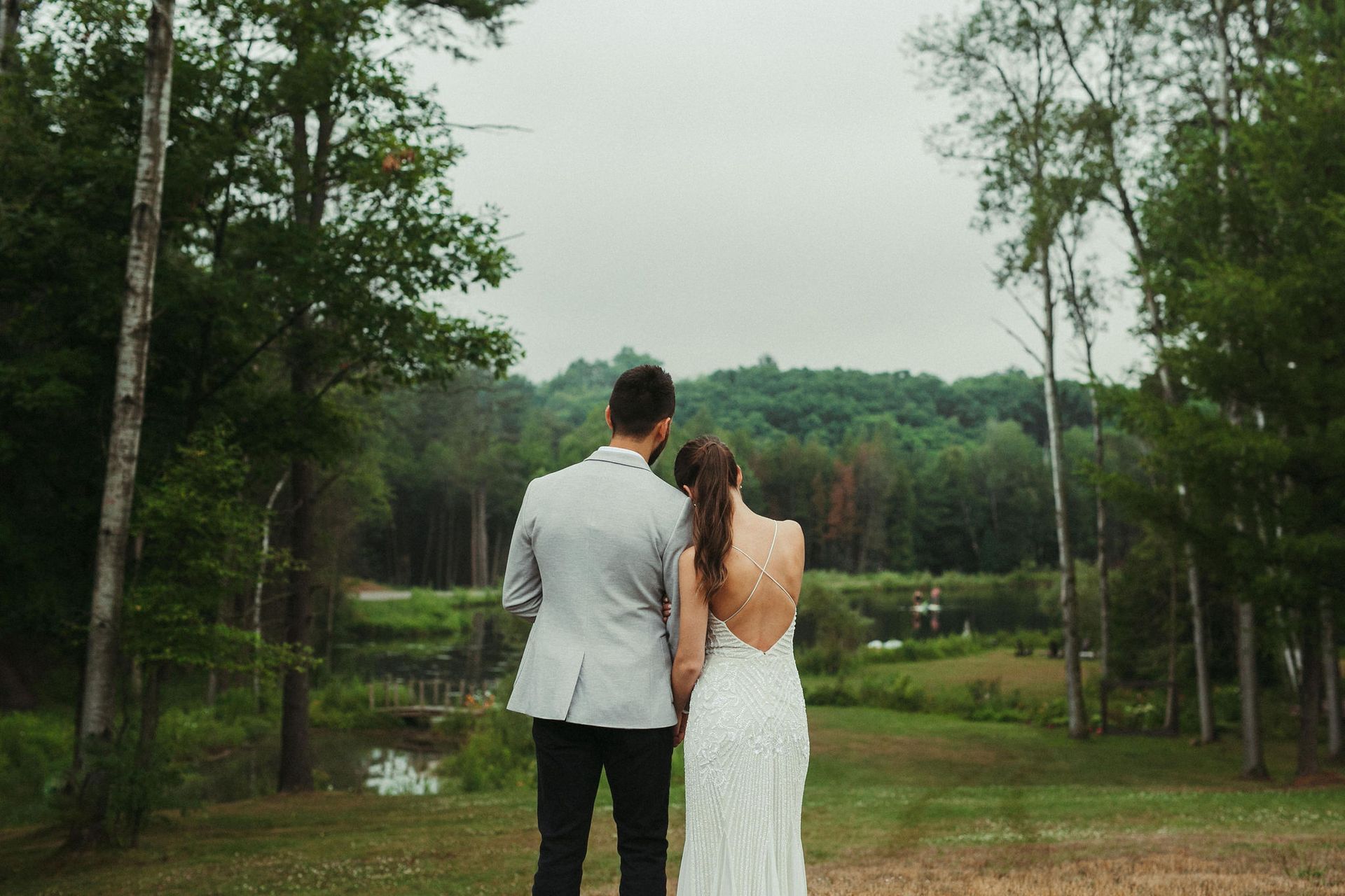 Couple in wedding attire looking out at a scenic forest view.
