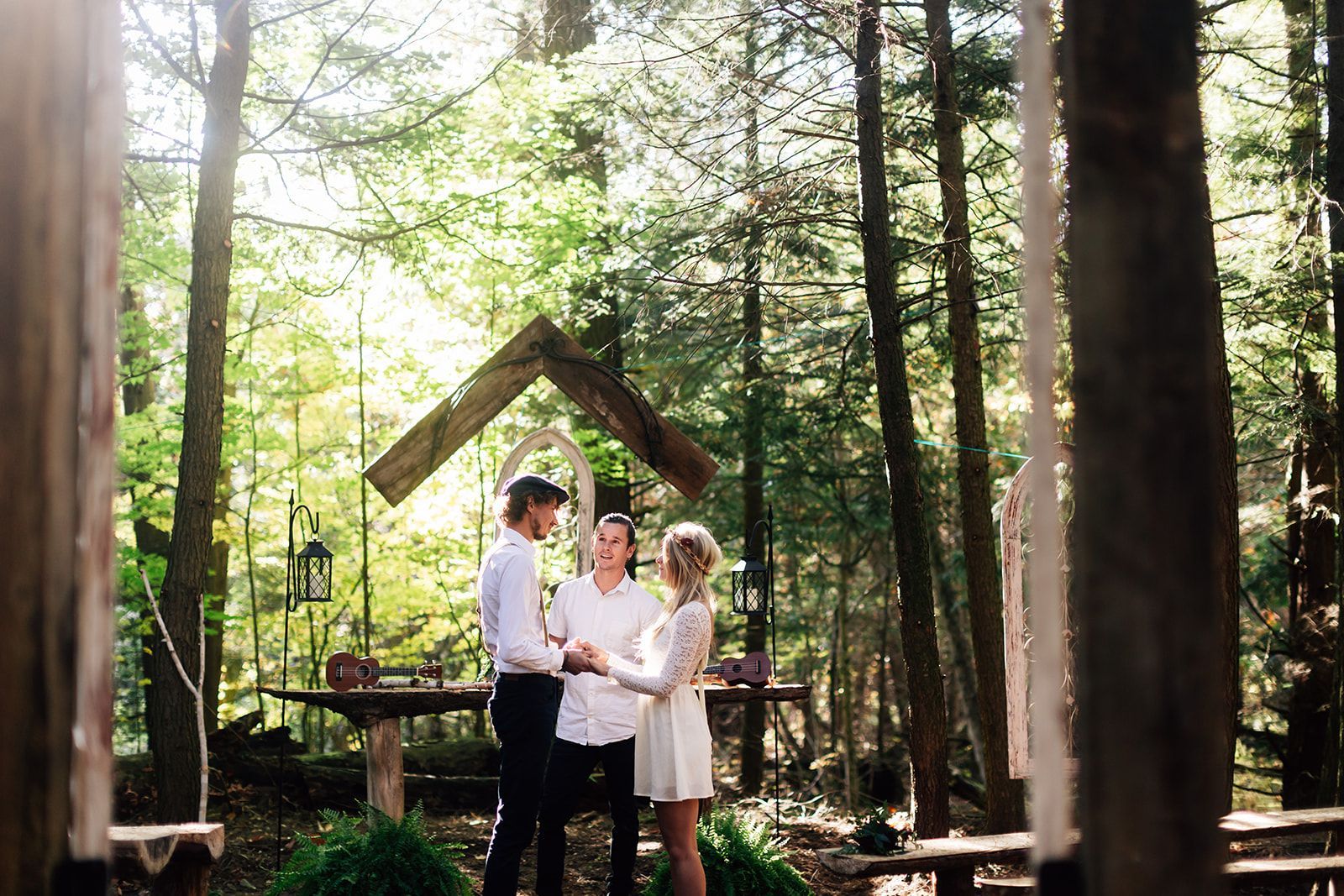 Couple exchanging vows at a forest wedding, officiant present. Sunlight through trees.