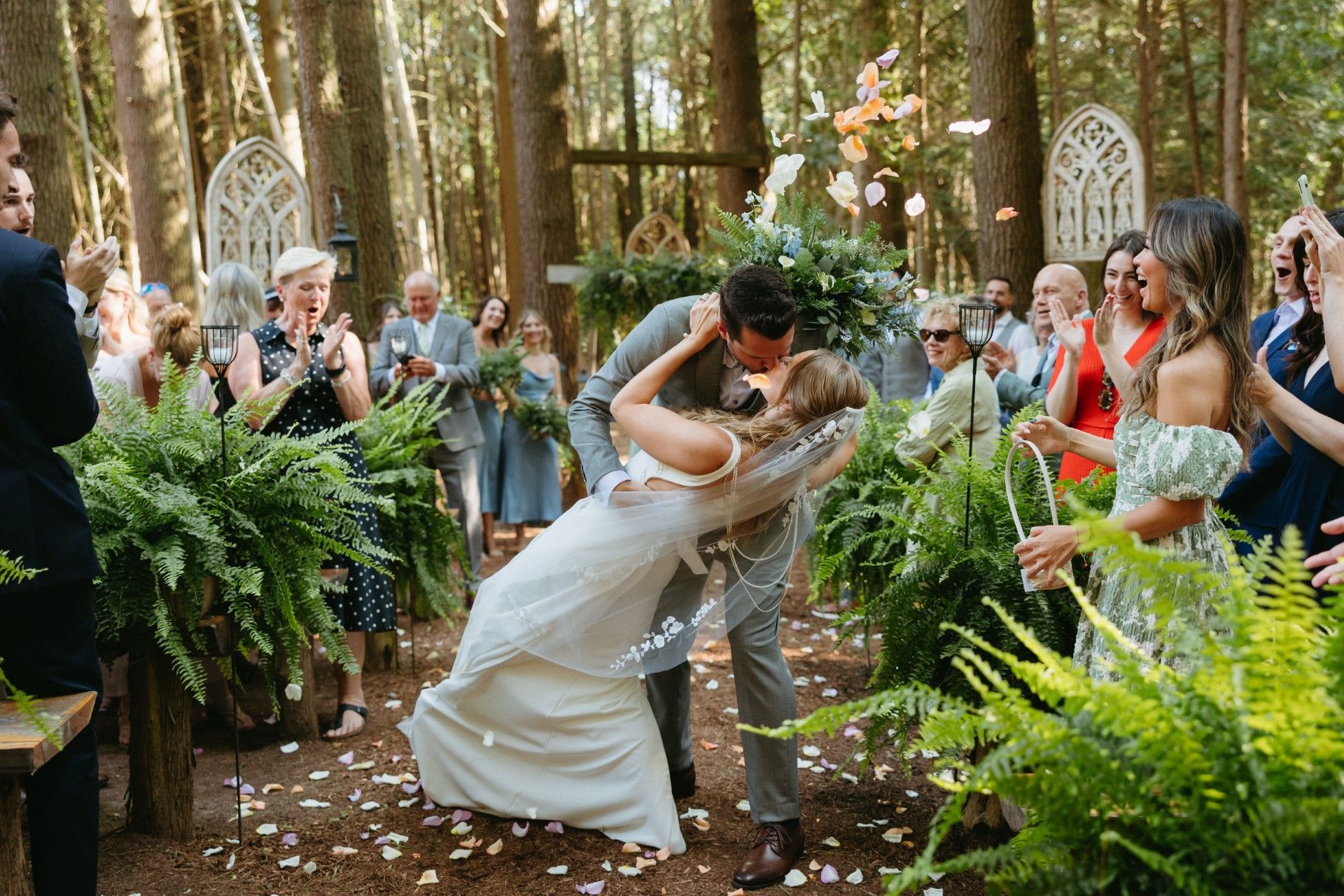 Bride and groom kissing outdoors in a forest wedding ceremony, surrounded by guests and greenery