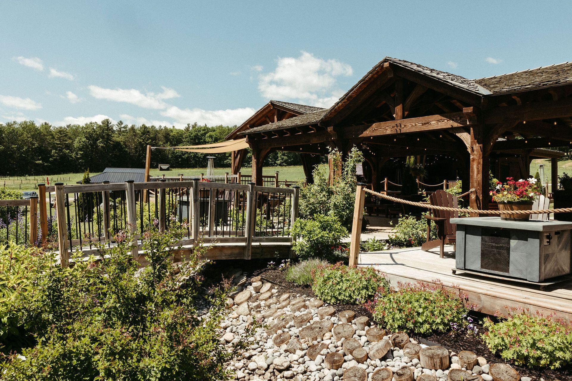 Outdoor patio at a vineyard with wooden structures, overlooking grapevines and greenery on a sunny day.