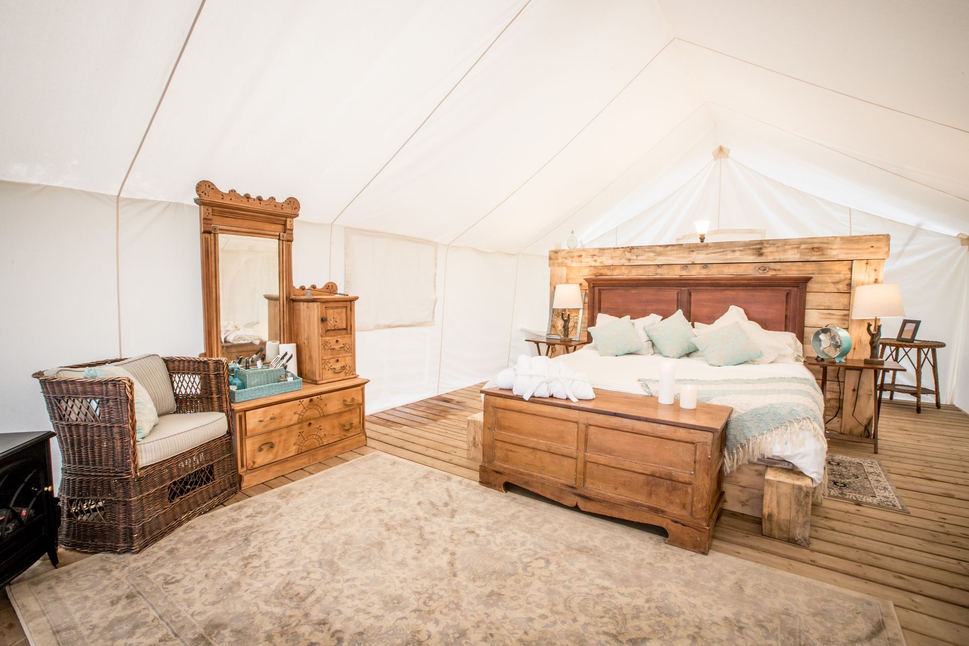 Spacious glamping tent interior with wooden furniture, bed, and neutral-toned rug.