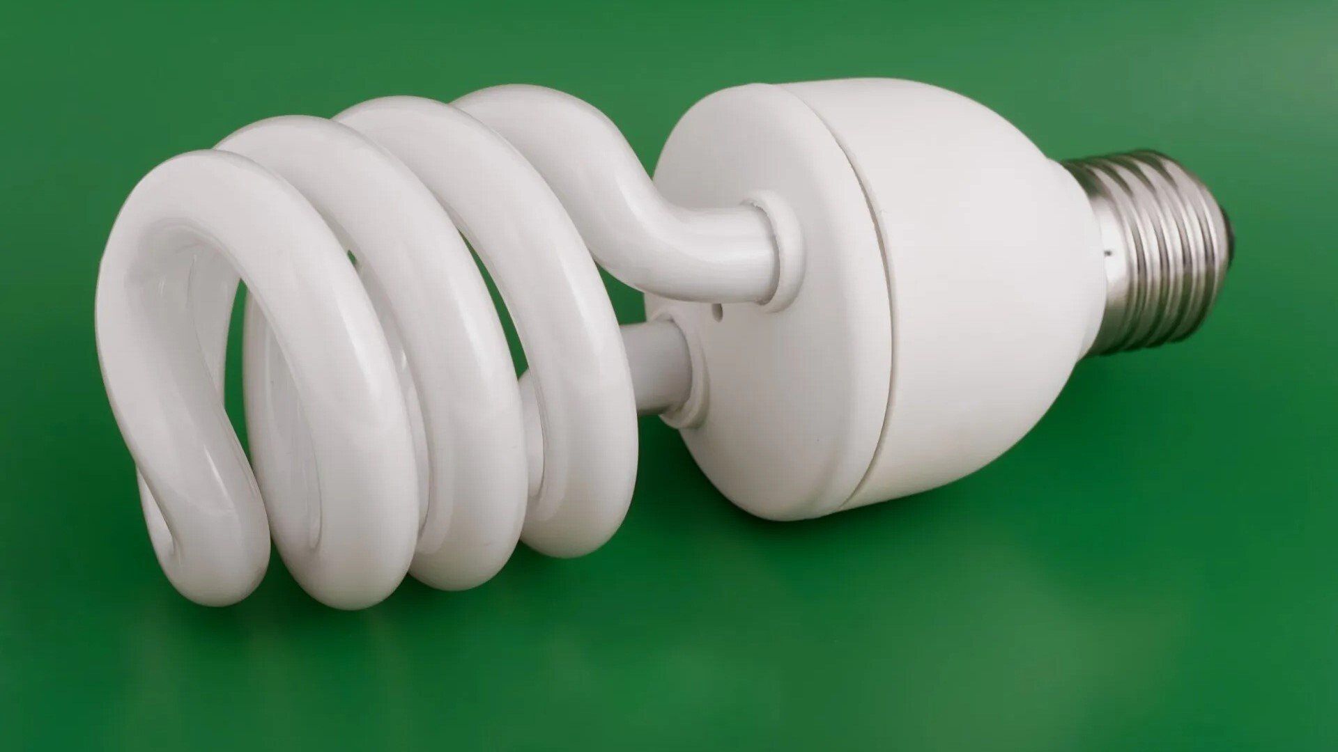 Bulb — Lewisville, TX — AAA Recycling, Inc. White, spiral-shaped CFL lightbulb on a green surface, with a silver base.