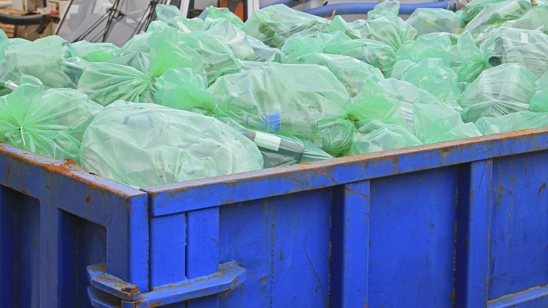 Concrete Debris — Lewisville, TX — AAA Recycling, Inc. Blue dumpster overflowing with green trash bags.