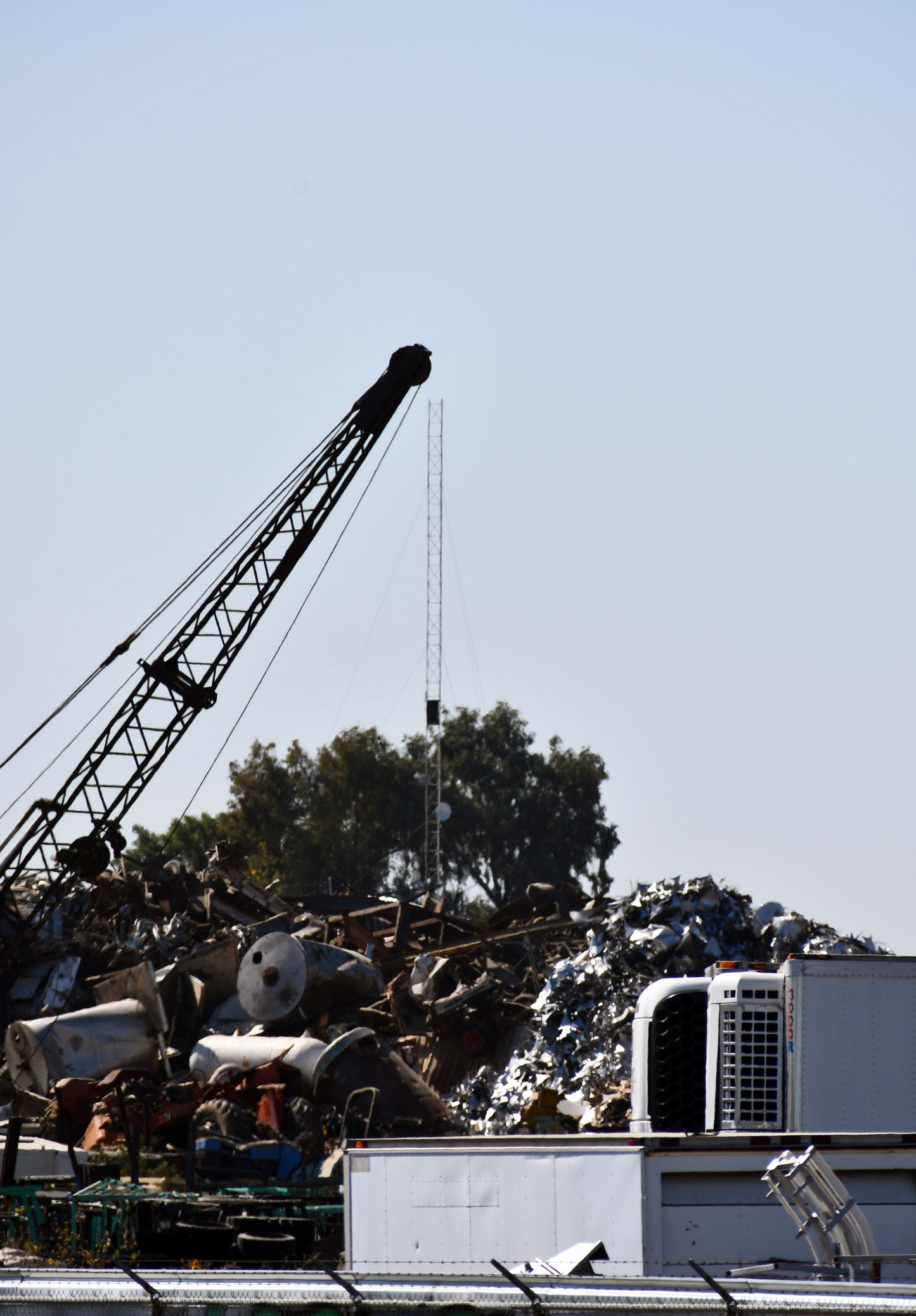 Crane lifting scrap metal in a junkyard under a clear sky.