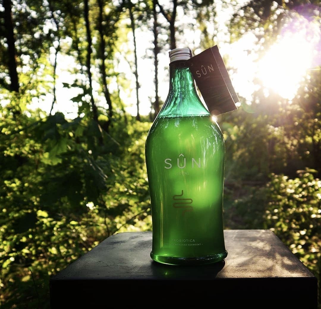 Fles gouden vloeibaar probiotica gember, eucalyptusbladeren en wortelschijfjes op een houten ondergrond