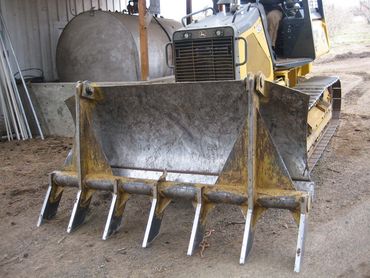 Yellow bulldozer with a front bucket and teeth parked in a shed, covered in dirt and wear