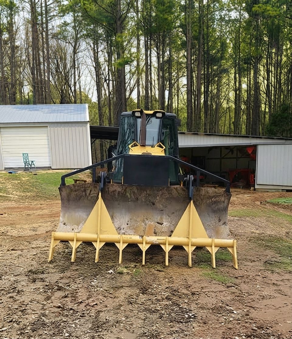 Front loader with yellow bucket attachment in a muddy yard near sheds and trees