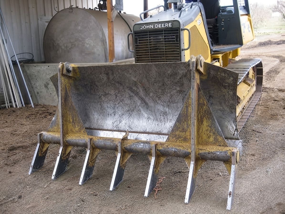 Yellow bulldozer with raised front bucket and ripper teeth in a dirt-covered shed