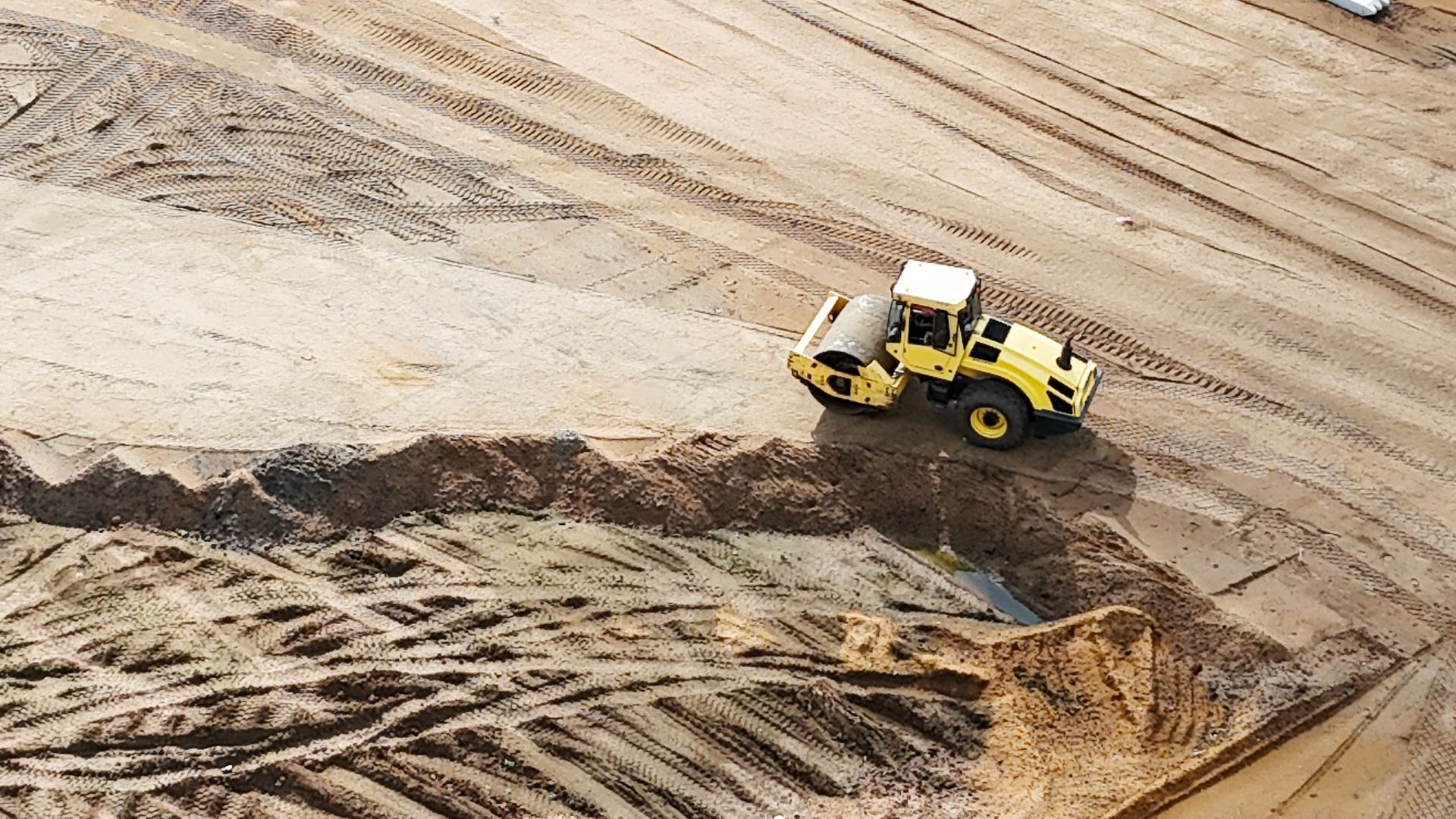 Yellow bulldozer clearing sand at a construction site, viewed from above.