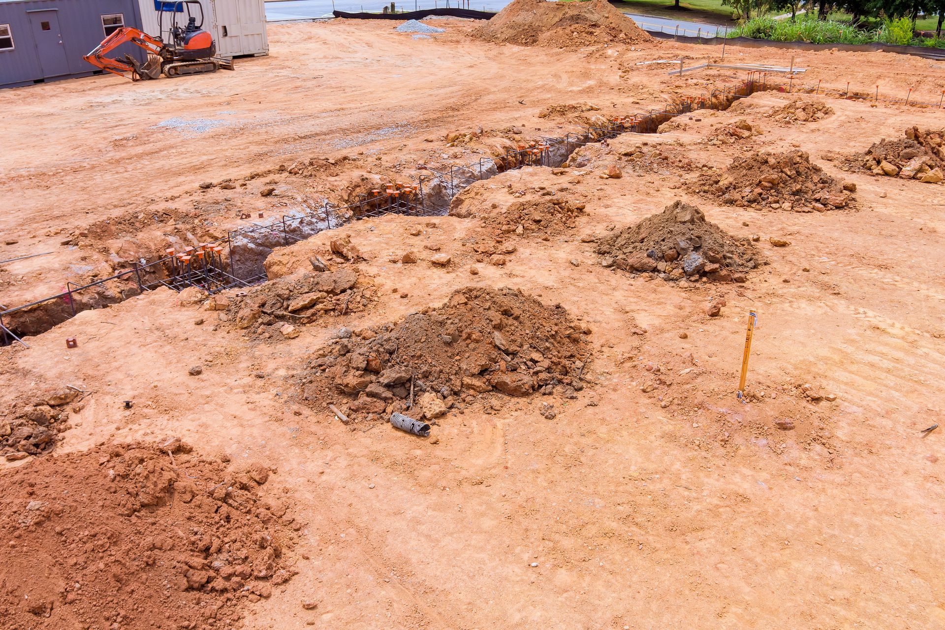 Excavated dirt piles on a muddy construction site near water and machinery