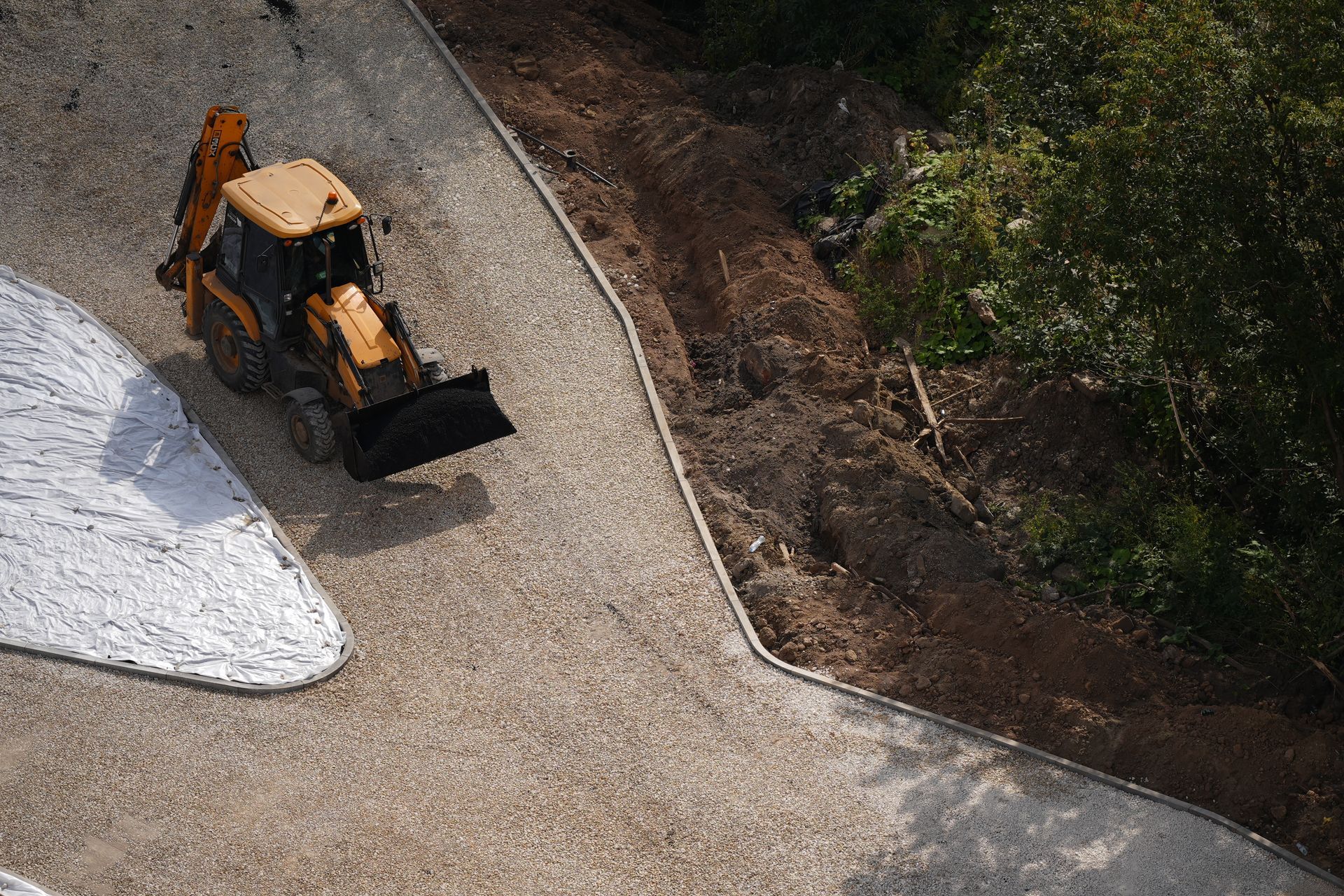Orange backhoe on a gravel path beside a white barrier and dirt embankment.