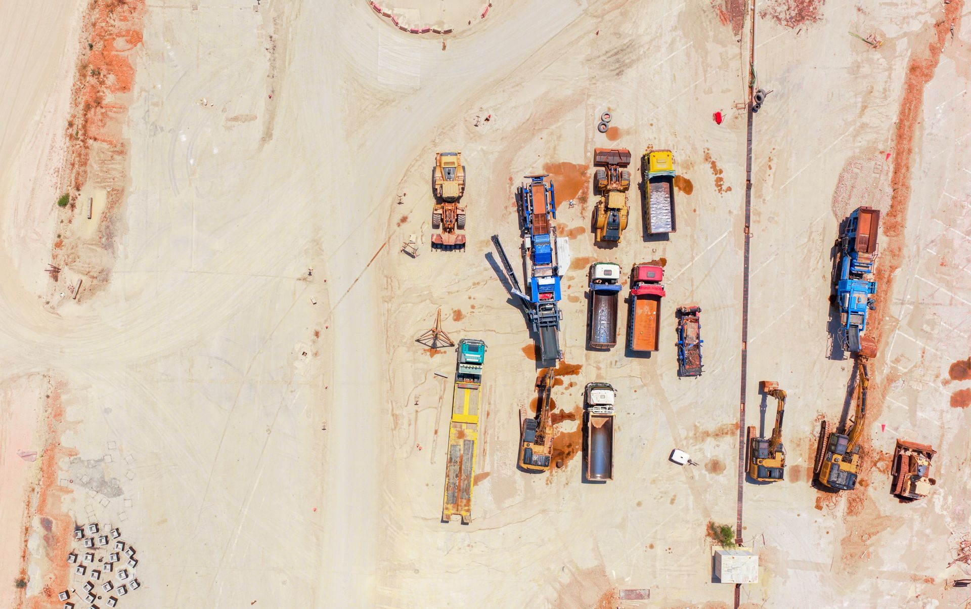 Aerial view of a construction site with several trucks and heavy machinery on a dirt lot.