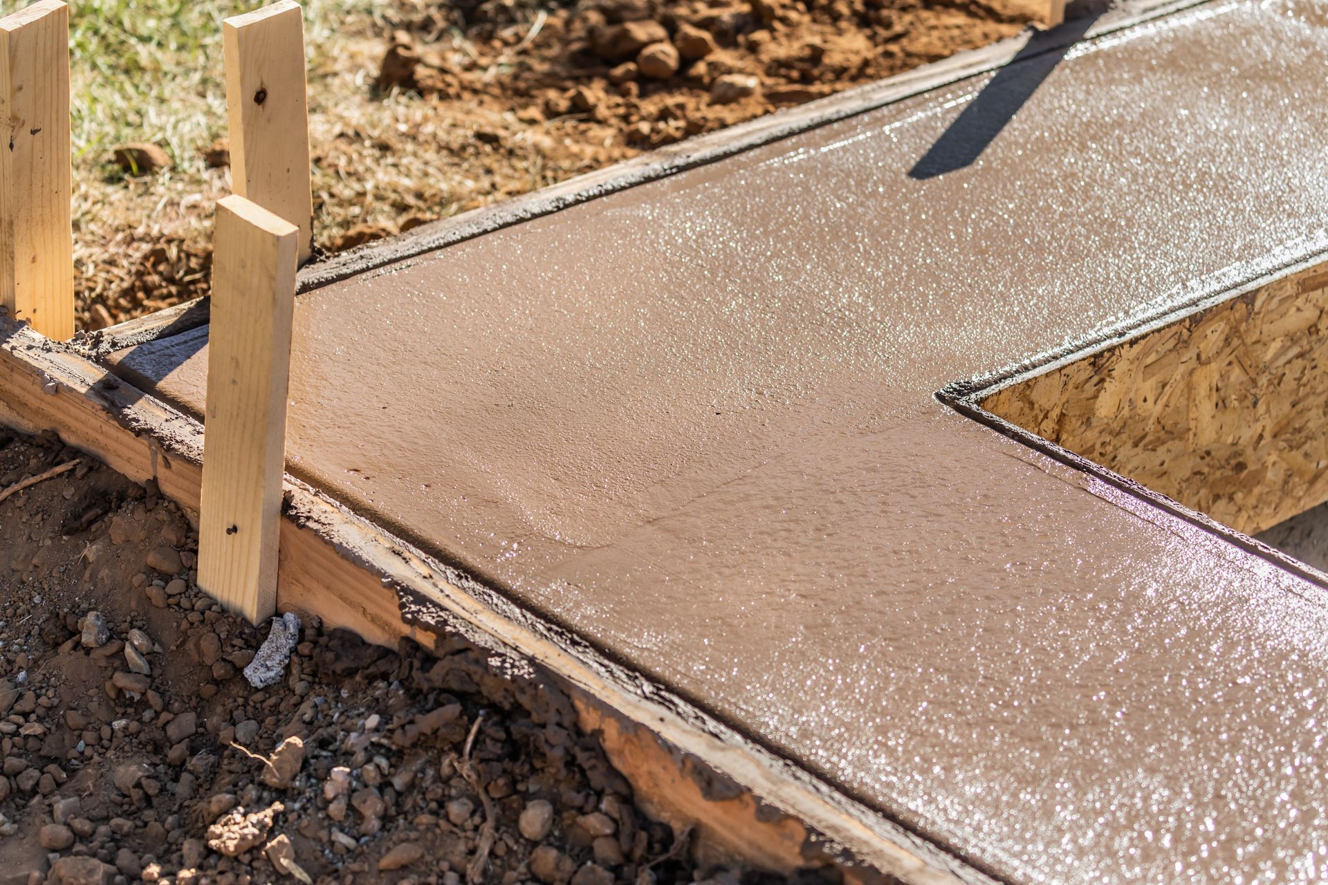 Fresh concrete sidewalk section with wooden forms at the edge of a dirt lot