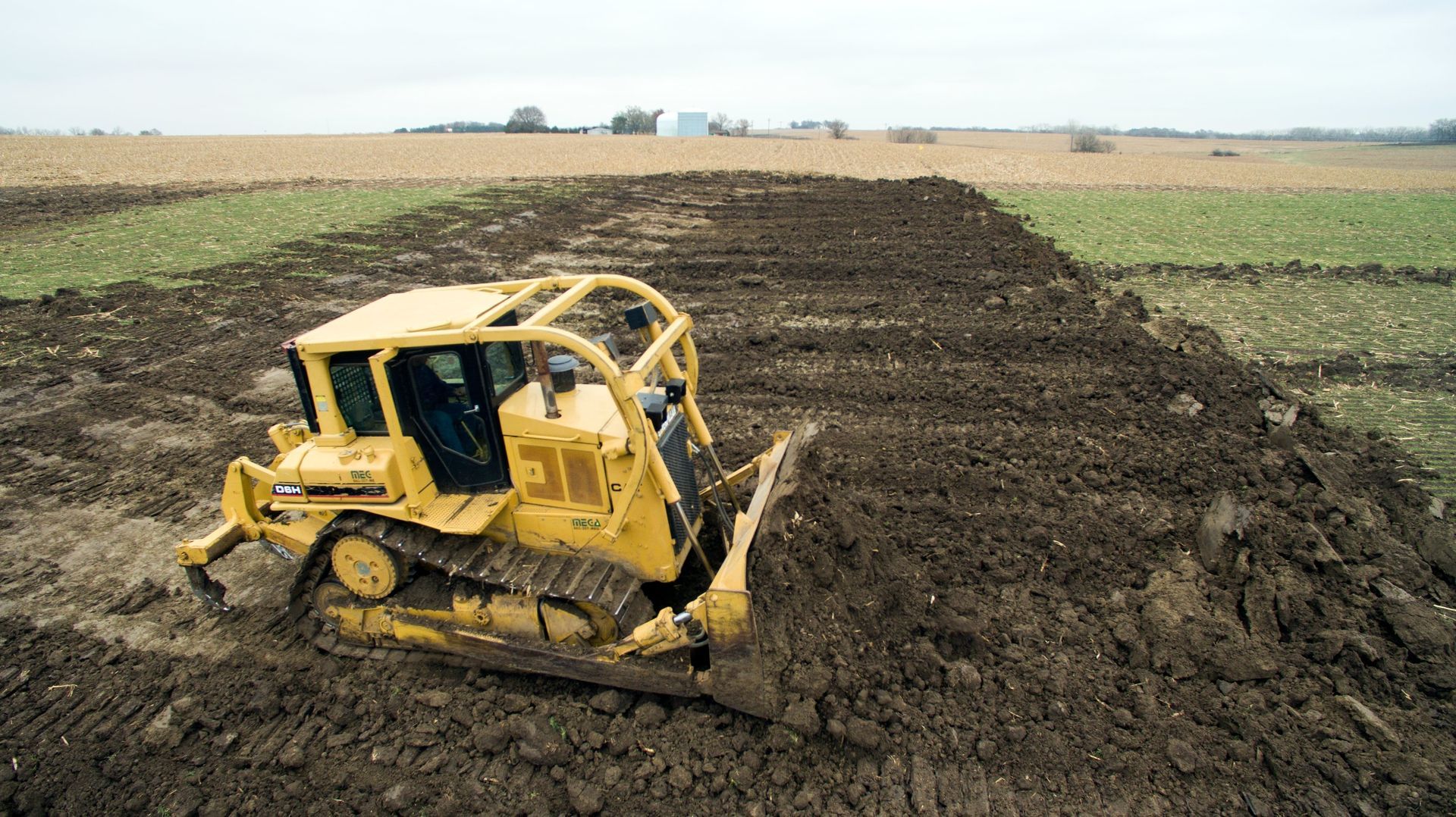 Old skid steer loader with bucket on gravel in a yard, autumn trees and fence in the background