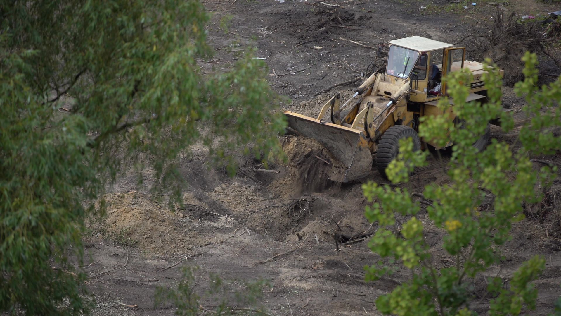 Yellow bulldozer clearing dirt on a wooded hillside trail
