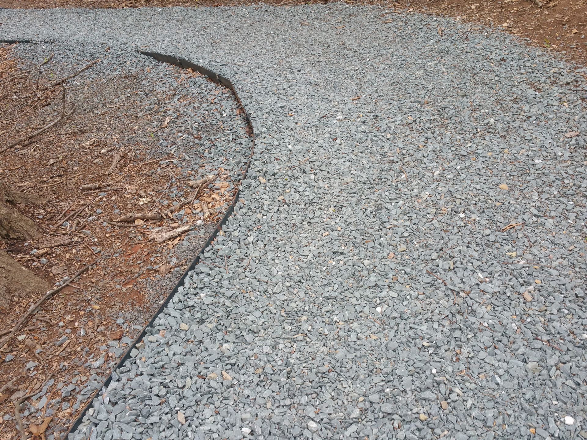 Curved gravel path beside a bare dirt area, showing a rough edge and textured ground