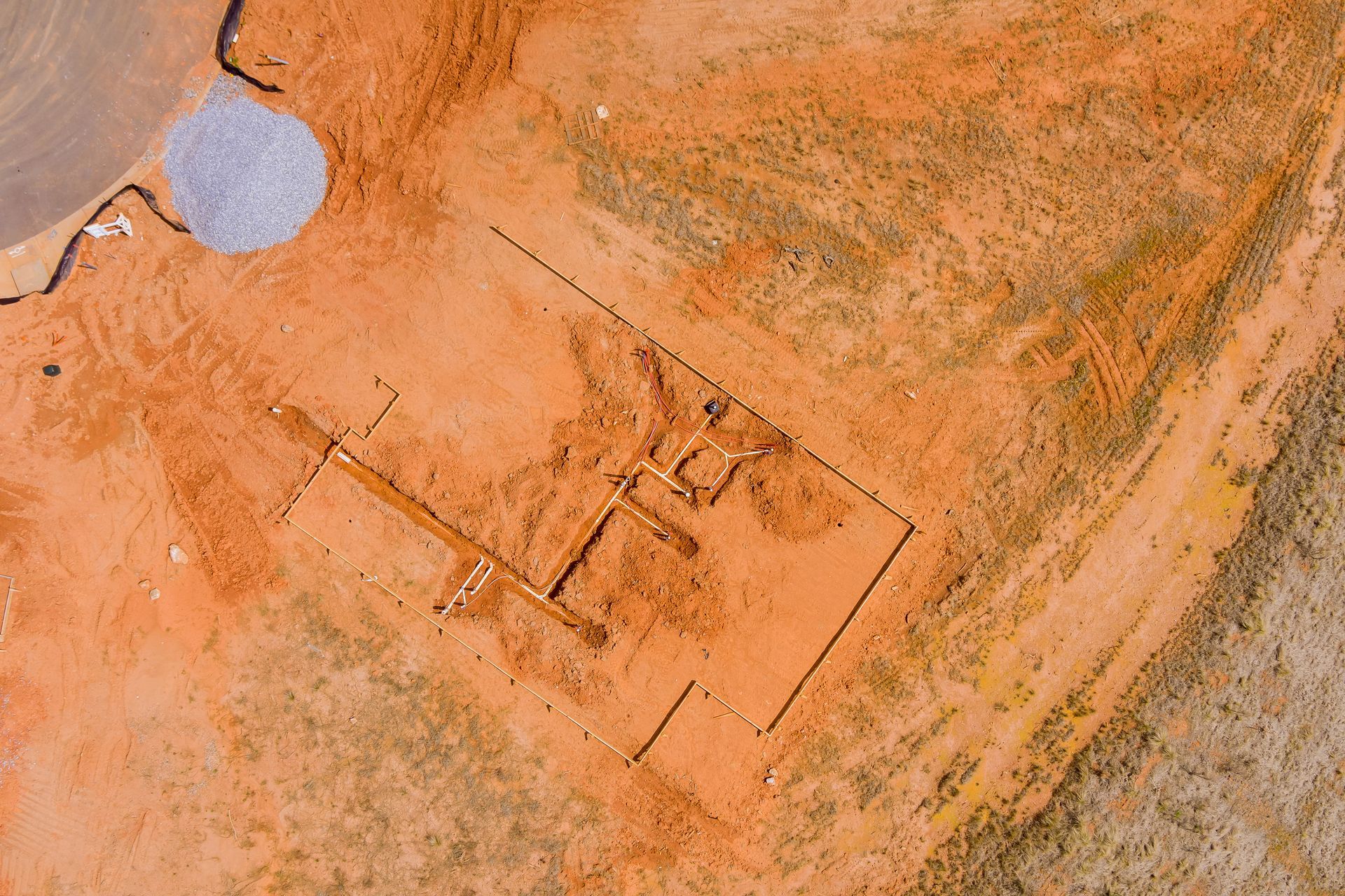 Aerial view of a reddish desert site with a rectangular excavation and a small pond nearby