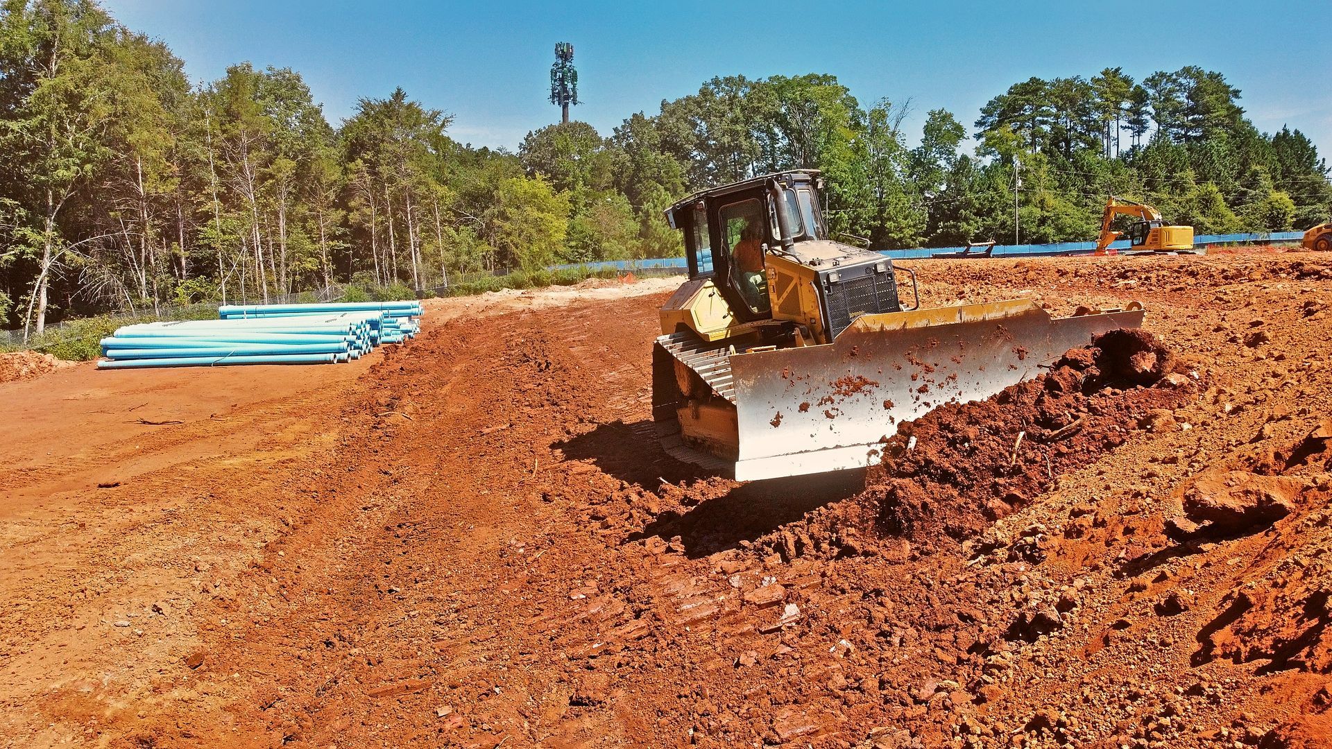 Bulldozer grading reddish dirt at a construction site with trees in the background