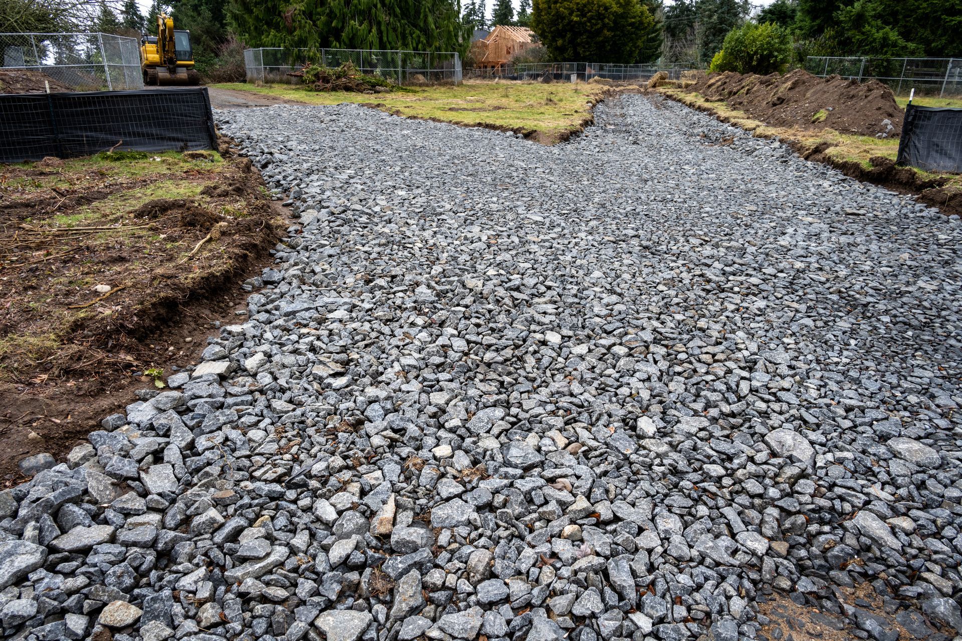 Gravel path under construction beside muddy ground, with a small excavator in the distance.