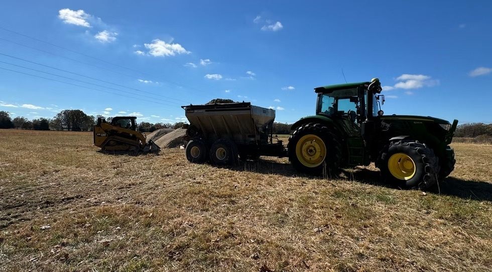 Tractor towing a grain cart in a harvested field under a blue sky