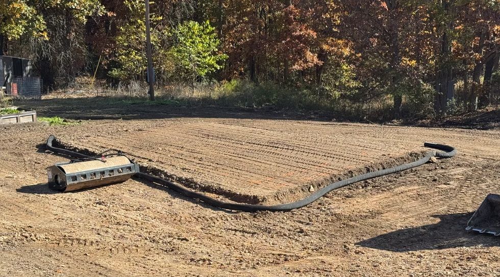 Black hose or pipe laid across a dirt field with a small metal platform, trees in the background