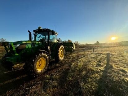 Green tractor in a frosty field at sunrise, with another tractor in the distance