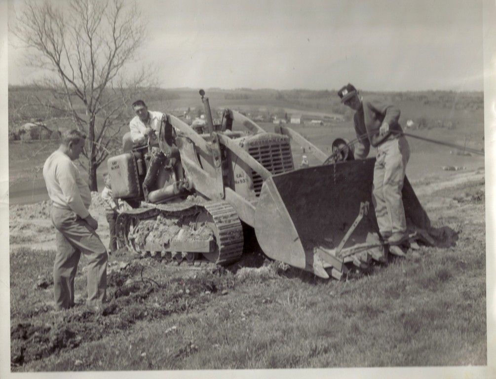 A group of men standing around a bulldozer in a field