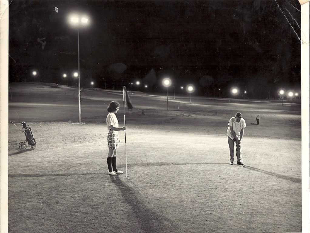 A black and white photo of two people playing golf at night