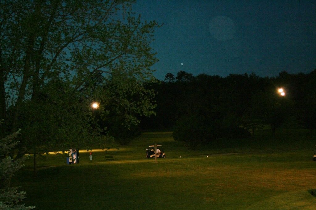 A group of people are sitting at a picnic table in a park at night.
