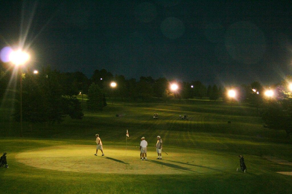 A group of people are playing golf at night on a golf course.