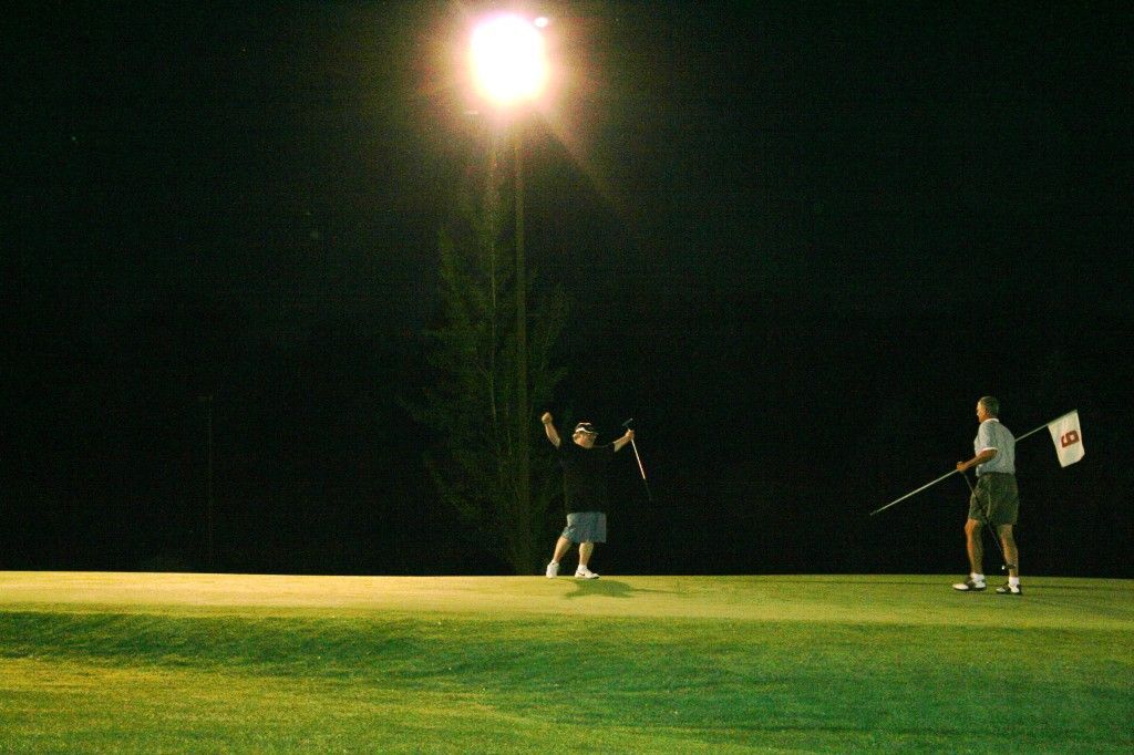 Two people are flying a kite on a golf course at night.
