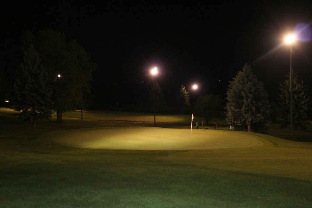 A golf course is lit up at night with trees in the background.